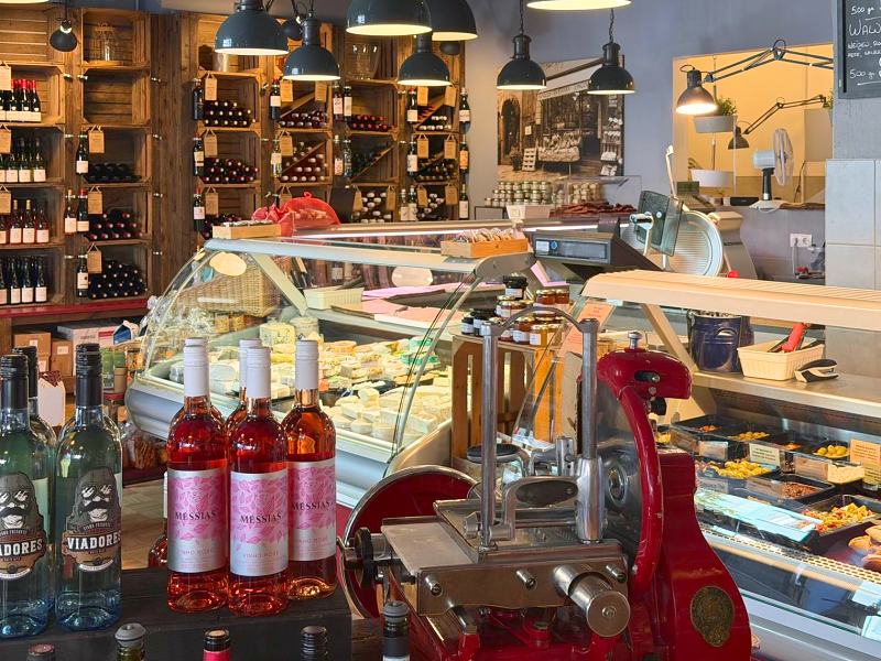 Theke mit roter Aufschnittmaschine, Roséweinen und Weinregalen im Hintergrund