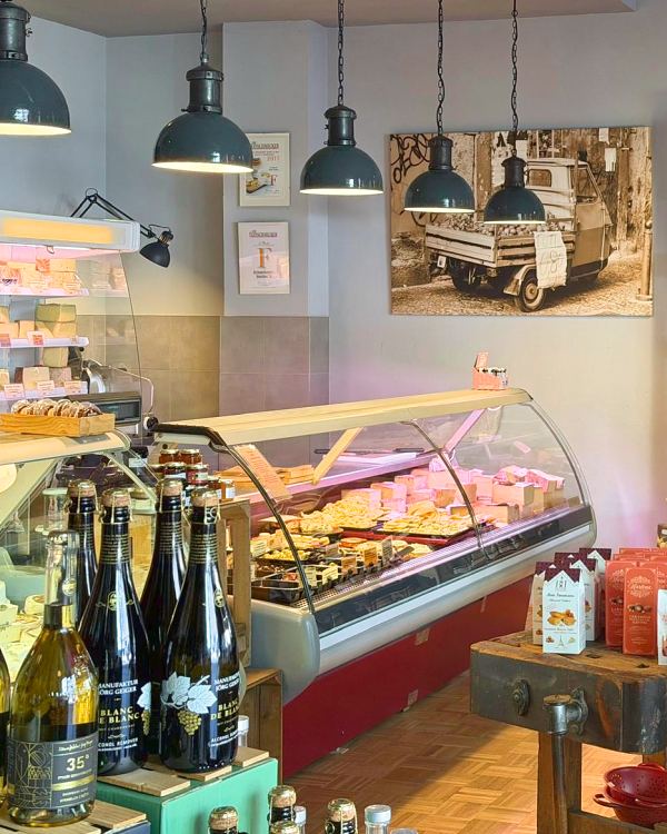Blick in den Laden mit Käsetheke, Hängelampen und einem Foto einer italienischen Ape an der Wand