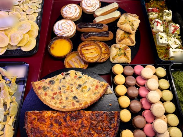 Theke mit Zitronen-Baiser-Tartes, Éclairs, Apfeltartelettes, Blätterteigtaschen, Quiche und Macarons